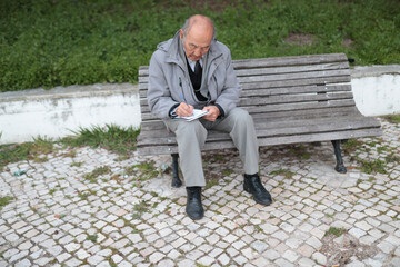 Obraz premium Senior professor writing notes outdoors on campus bench