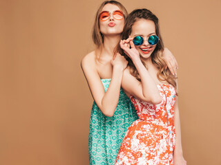 Two young beautiful blond smiling hipster female in trendy summer dresses. Sexy carefree women posing near golden wall in sunglasses. Positive cute models hugging