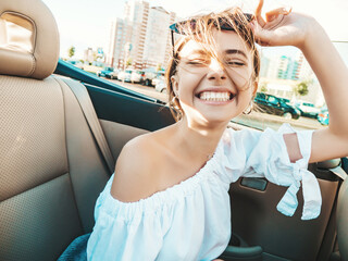 Portrait of young beautiful and smiling hipster female in convertible car. Sexy carefree woman...