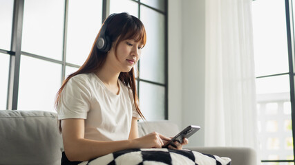 Asian woman wearing headphone listen to music and using smartphone choose playlist