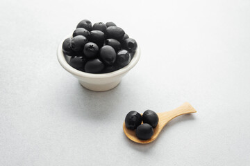 Black olives in white bowl and wooden spoon on bright background