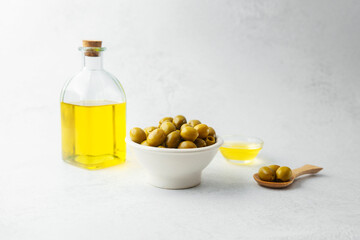 Green olives in bowl with glass bottle and oil on light background