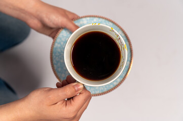 A cup of freshly brewed coffee held in the hands of a woman on a gray background, Woman holding a...