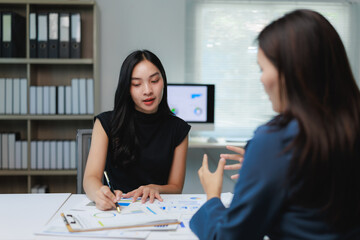 Two businesswomen discussing charts and analyzing statistics in office meeting