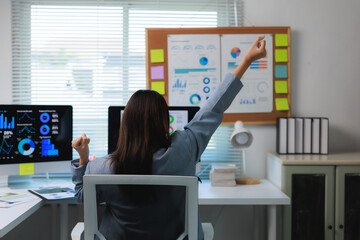 Businesswoman celebrating success while working with financial charts on computer in office