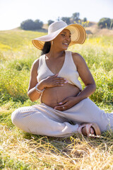 A beautiful pregnant woman enjoying a delightful sunny day outdoors, completely surrounded by nature, and embodying pure joy and serenity throughout her pregnancy journey and experience