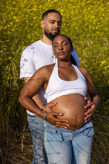 A loving African American couple is blissfully enjoying the summer outdoors, celebrating their joyous pregnancy amidst a beautiful and vibrant natural setting filled with greenery and sunshine