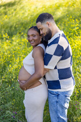 On a summer day, a loving African American couple cherishes the moment outdoors, surrounded by greenery, joyfully celebrating their pregnancy and embracing their journey together with warmth