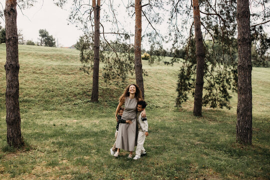 Happy mother walking with her two sons in a sunny forest meadow.
