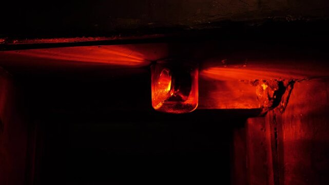 Close-up of a rotating red emergency siren lamp on the wall of a dark tunnel. A bomb shelter, an emergency signal on the wall during an air raid.