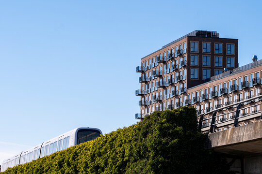 Low-angle shot of a metro train crossing between contemporary buildings in &Oslash;restad, Copenhagen, under clear sky and sharp geometry for themes of design and urban transit systems.