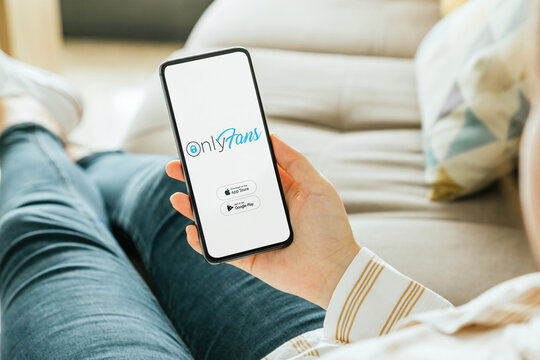 Woman relaxing on sofa holding smartphone with onlyfans app open