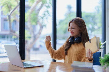 An excited woman celebrates success while working from home with laptop.