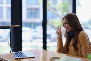 Obraz premium Young woman makes peace sign du a video call on her laptop indoors.