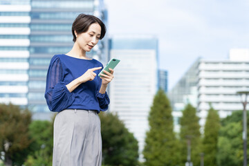 Fototapeta premium ビル街でスマートフォンを操作している女性