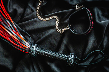 Leather whip and handcuffs on black fabric - bdsm accessories with chains and flogger