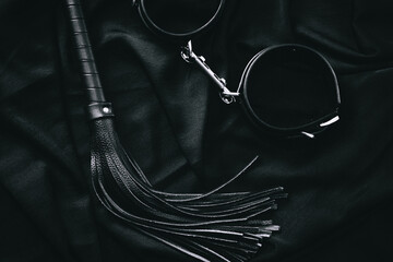 Black leather whip and handcuffs on dark background - bdsm accessories display