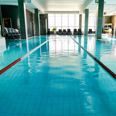 An indoor swimming pool in a sports club, surrounded by relaxation areas and large windows allowing natural light.