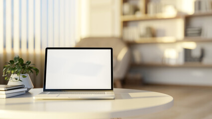 White screen laptop at a round table on wooden floor of living room with large bookshelf or library.