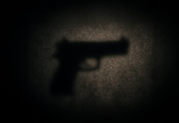 Silhouette shadow of a handgun cast against a dimly lit textured wall, evoking tension and symbolic threat under low light.