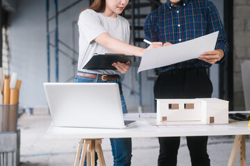 Asian couple reviews architectural plans together at renovation site. They collaborate on ideas to...
