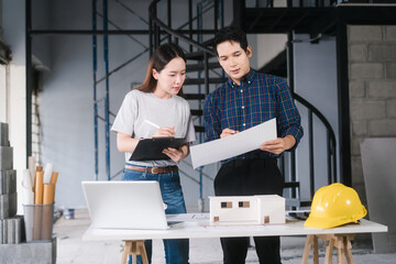 Asian couple reviews architectural plans together at renovation site. They collaborate on ideas to...