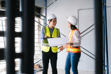 Asian male and female engineers wearing safety vests and helmets inspect structural elements,...