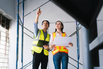 Asian male and female engineers wearing safety vests and helmets inspect structural elements,...