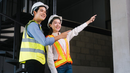 Asian male and female engineers wearing safety vests and helmets inspect structural elements,...