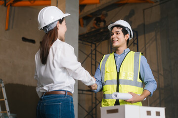 Asian male and female engineers wearing safety vests and helmets inspect structural elements,...