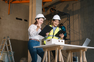 Asian male and female engineers wearing safety vests and helmets inspect structural elements,...