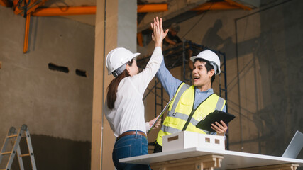Asian male and female engineers wearing safety vests and helmets inspect structural elements,...