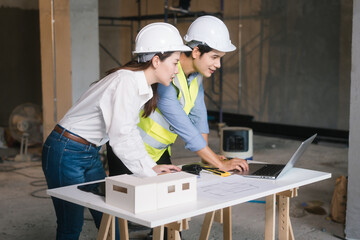 Asian male and female engineers wearing safety vests and helmets inspect structural elements,...