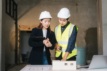 Asian male and female engineers wearing safety vests and helmets inspect structural elements,...