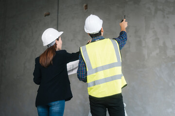 Asian male and female engineers wearing safety vests and helmets inspect structural elements,...