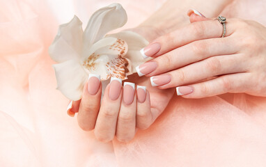 Woman showing french manicure holding white orchid on pink background