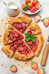 Delicious homemade strawberry galette with almond flakes being sliced on baking paper