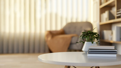 Books and potted plants on a round table in a living room or study room with armchair and bookshelf.