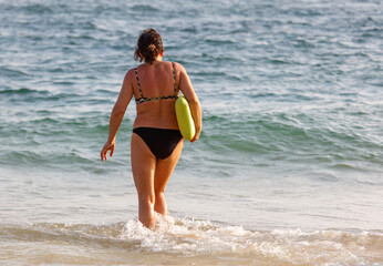 A woman is walking on the beach with a green buoy in her hand