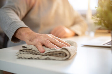 Close up of old white caucasian man hand holding a cloth rag cleaning or wiping dust on white table.