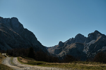 Grassy trail at the foot of Komovi peaks in Montenegro. Peaceful autumn landscape with dramatic alpine backdrop under a deep blue sky.