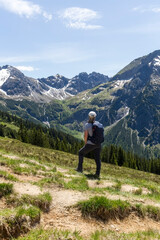 Eine Wanderin auf einem Bergpfad über grüne Hänge mit Blick in die weite, schneebedeckte...