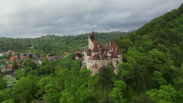 Aerial view: Majestic Bran Castle, also known as Dracula's Castle, stands on a hilltop surrounded by a dense forest in Transylvania, Romania