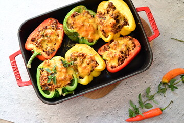 Close-up of vibrant stuffed bell peppers filled with seasoned ground beef, bulgur, and melted cheese. The dish is baked and served in a red baking dish placed on a blue rustic  food background. yummy