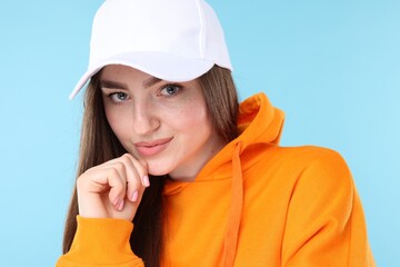 Portrait of beautiful woman in stylish baseball hat on light blue background, closeup