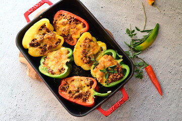 Close-up of vibrant stuffed bell peppers filled with seasoned ground beef, bulgur, and melted cheese. The dish is baked and served in a red baking dish placed on a blue rustic  food background. yummy