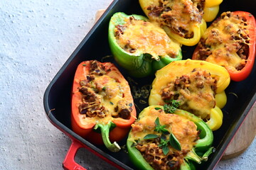 Close-up of vibrant stuffed bell peppers filled with seasoned ground beef, bulgur, and melted cheese. The dish is baked and served in a red baking dish placed on a blue rustic  food background. yummy