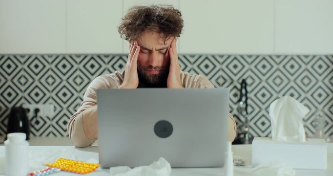 Frustrated man suffering from headache at home work. Exhausted tensed worker coping with migraine, emotional stress concept feeling pain sitting at office homa desk with laptop.