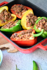 Close-up of Mediterranean-style stuffed bell peppers arranged in a red baking dish, ready for the oven. This homemade meal scene on a light background captures the essence of fresh, flavorful cooking