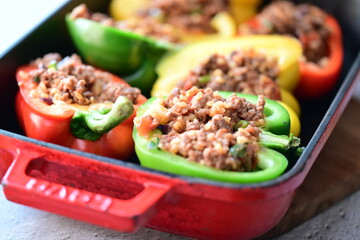 Close-up of Mediterranean-style stuffed bell peppers arranged in a red baking dish, ready for the oven. This homemade meal scene on a light background captures the essence of fresh, flavorful cooking